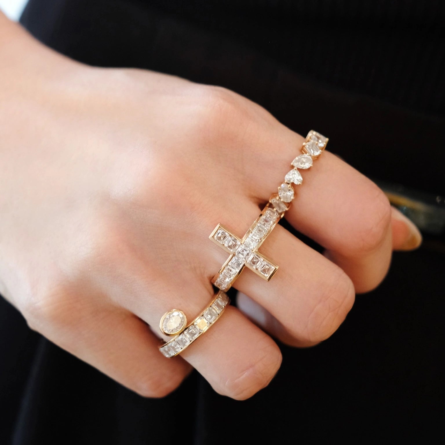 Hand wearing multiple gold rings with diamond accents on dark background