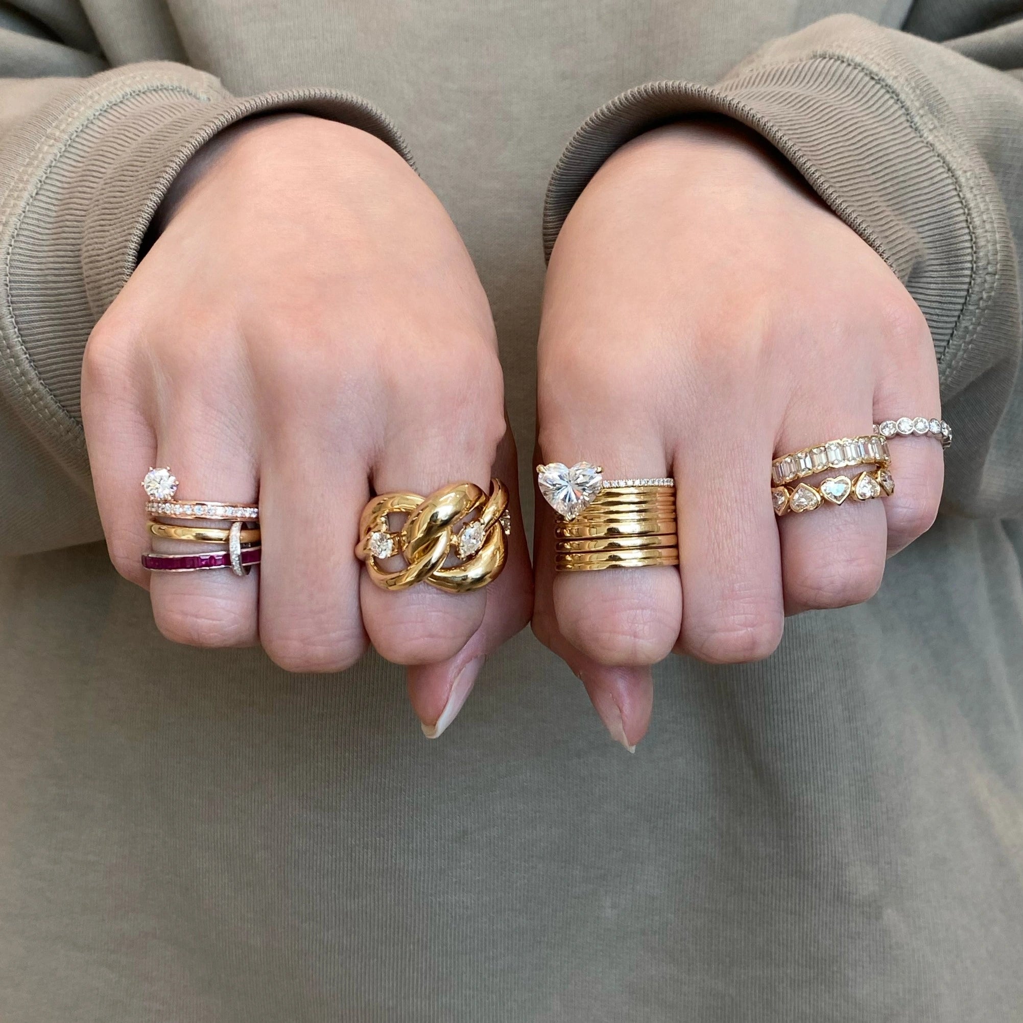Two hands wearing multiple gold and diamond rings