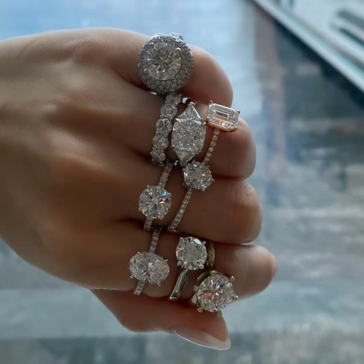 Hand wearing a collection of engagement rings with sea background.