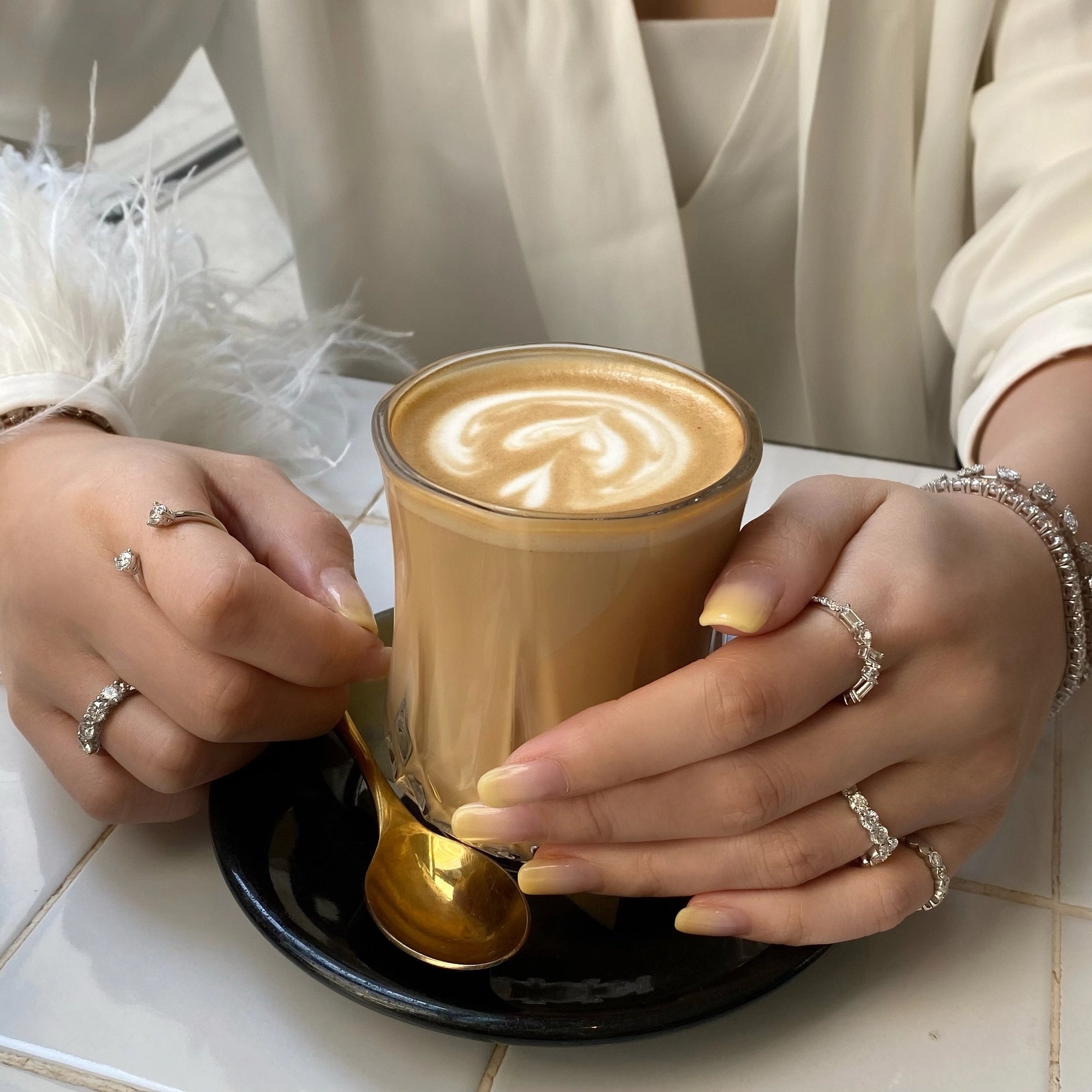 Wearing multiple diamond rings, a cup of coffee with latte art on a white surface