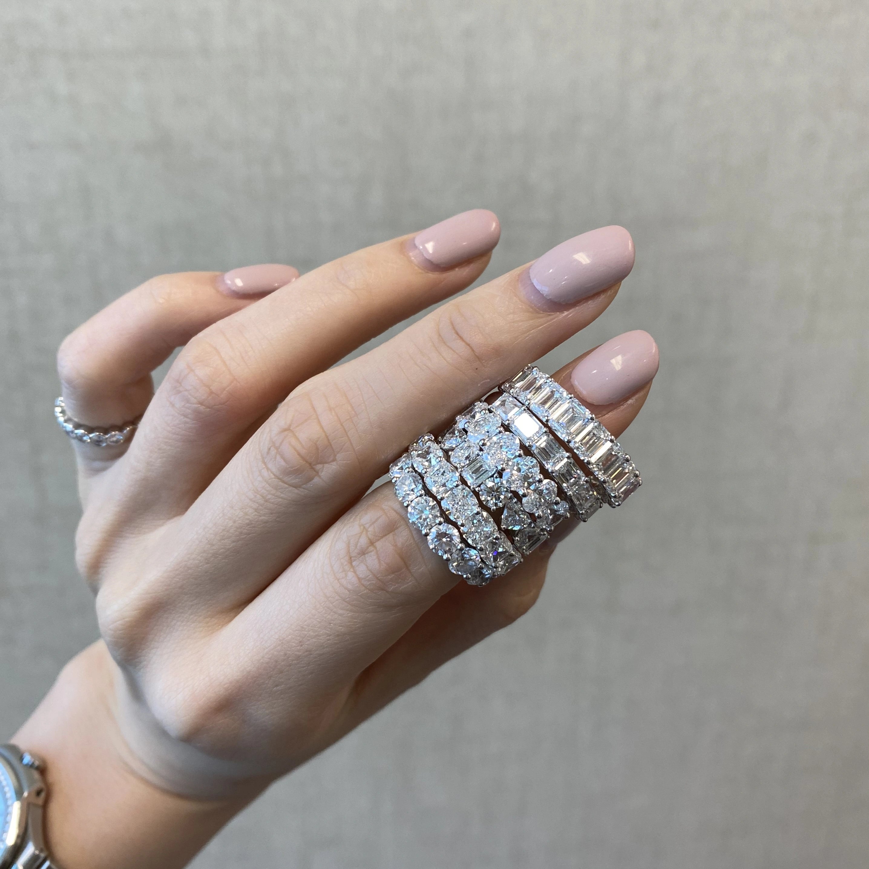 Hand wearing multiple diamond rings on a neutral background