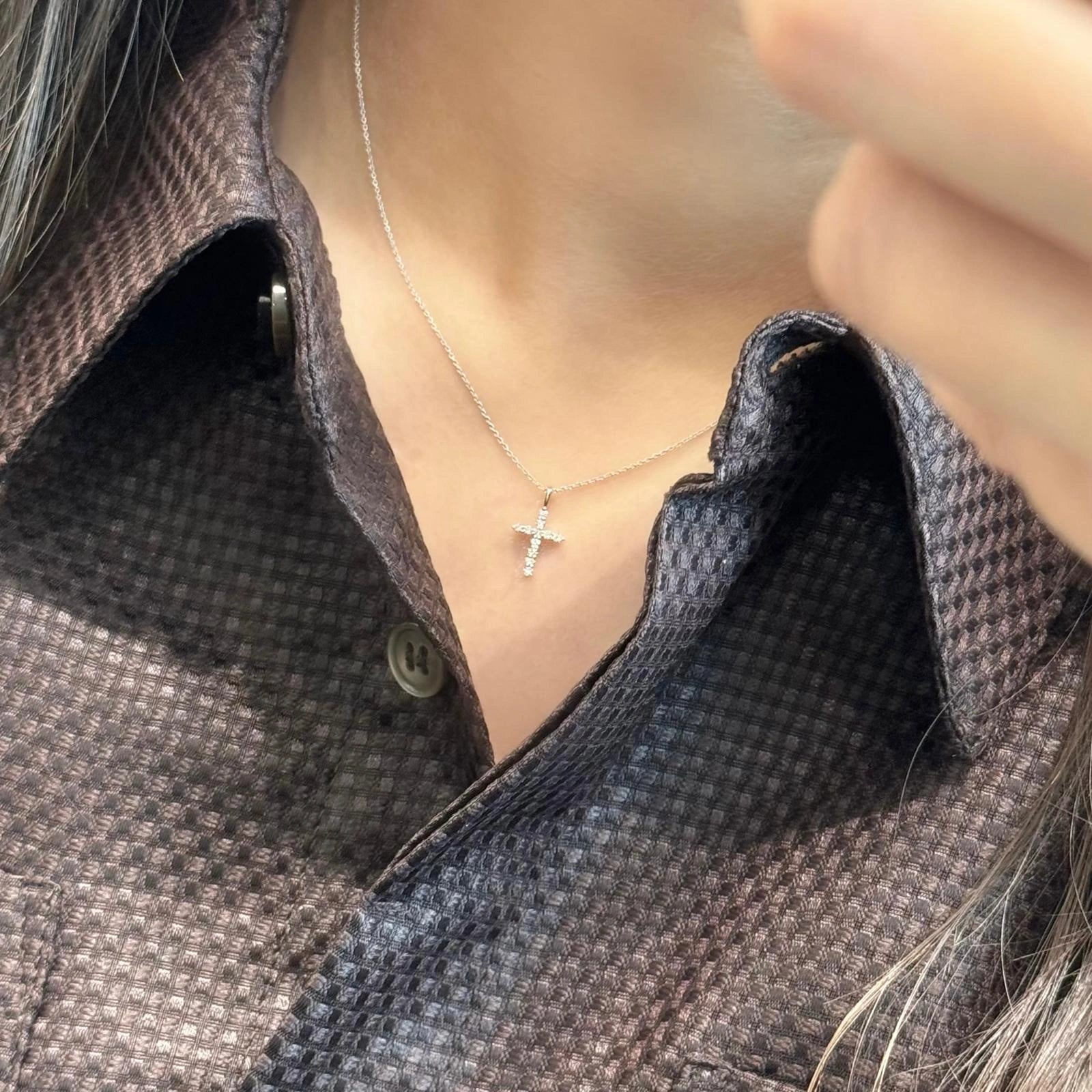 Necklace with a cross pendant worn by a person in a textured shirt.