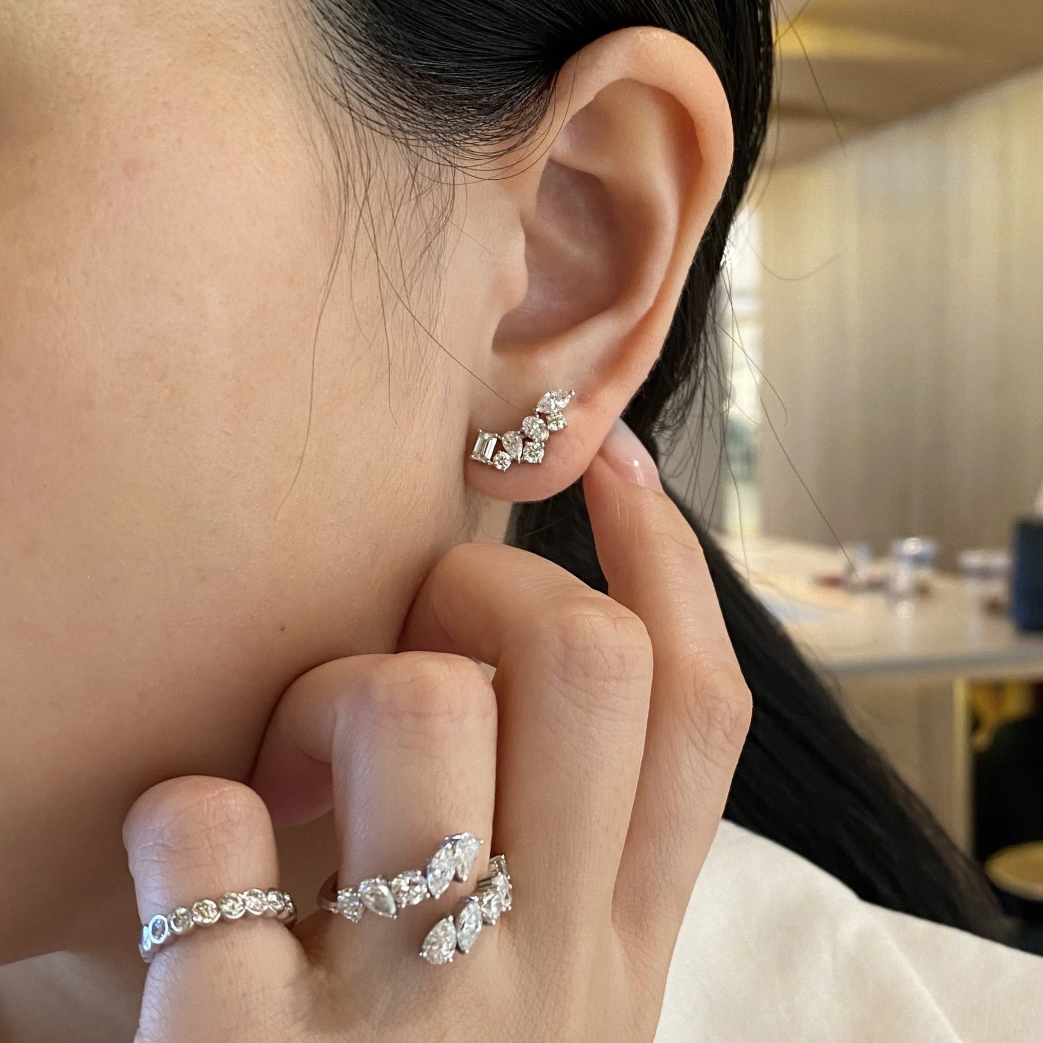Close-up of a person wearing diamond earrings and rings with a blurred indoor background