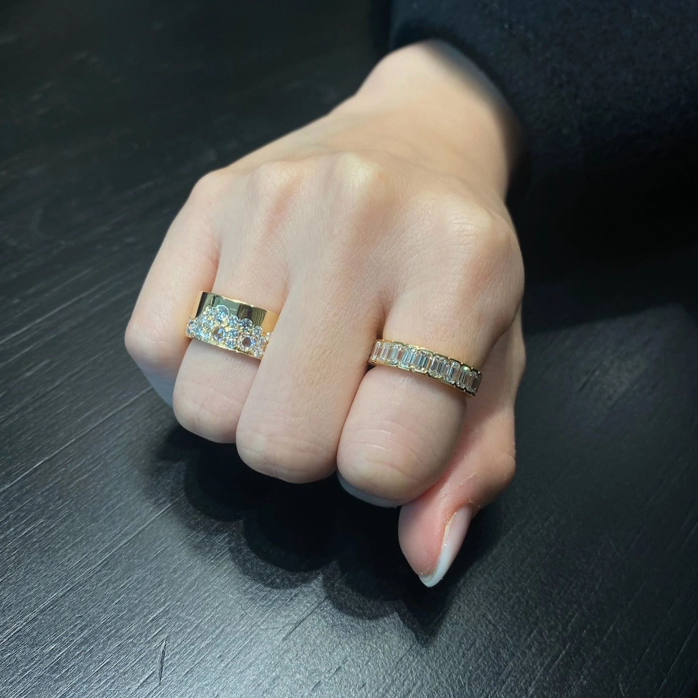 Hand wearing two rings on a dark surface