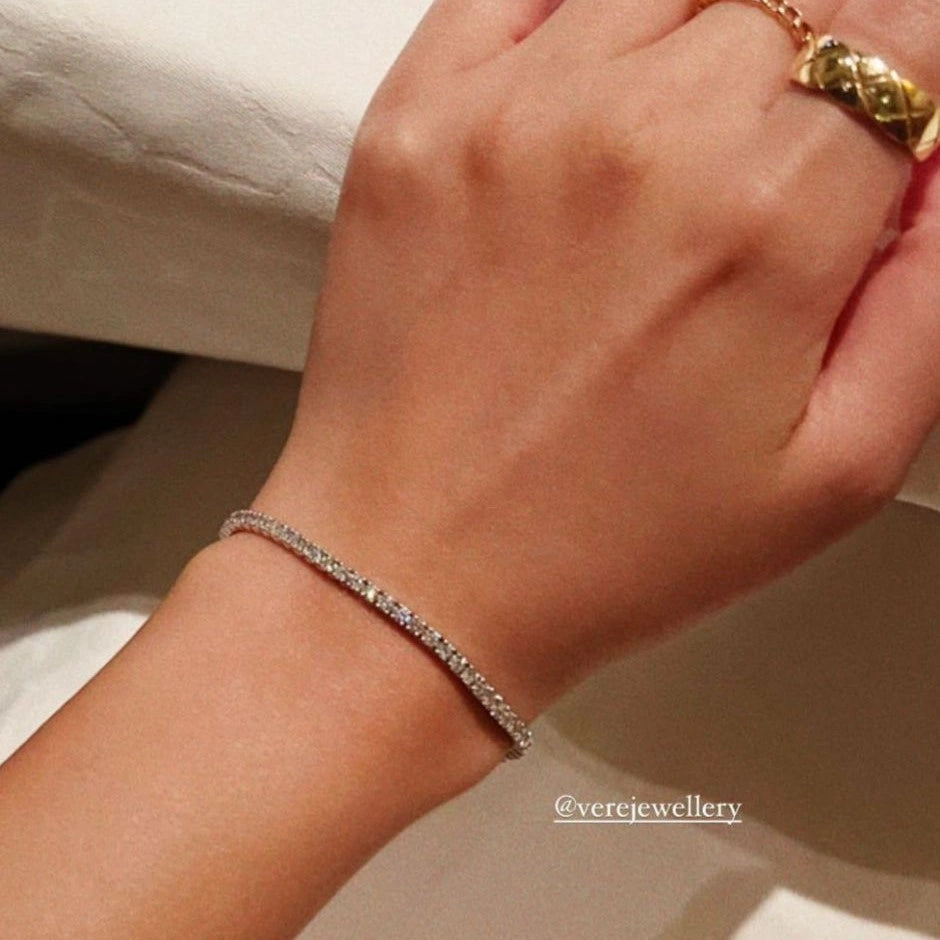 Hand wearing a tennis bracelet with a gold ring.