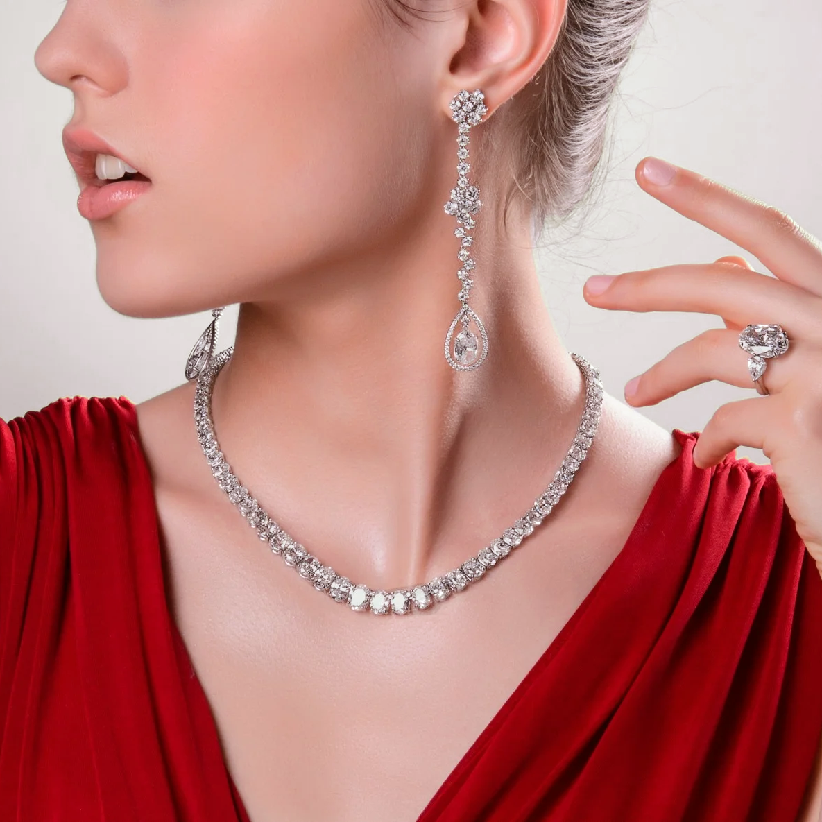 Woman wearing a gradual oval diamond necklace, in matching oval earrings, and ring for bridal look