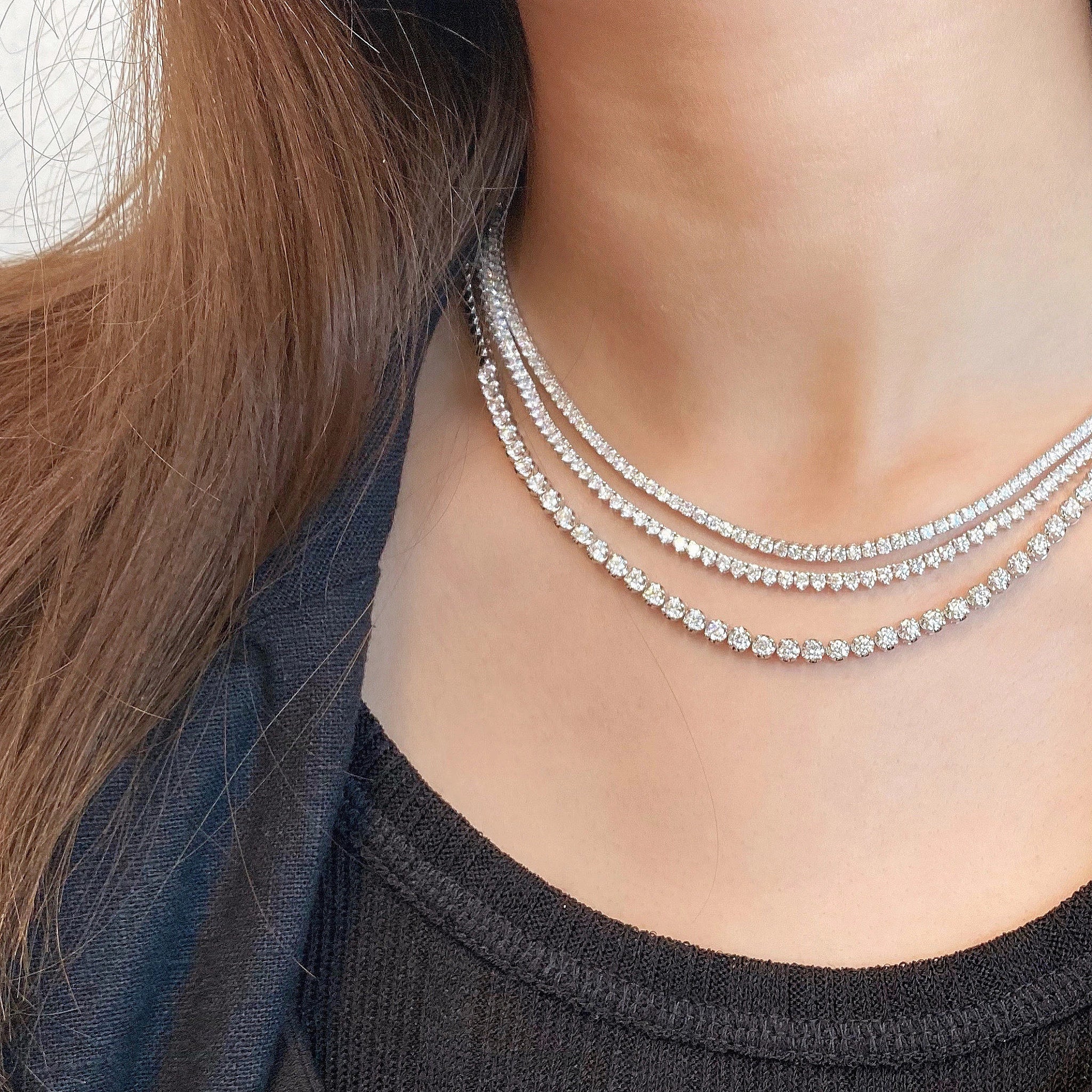 Close-up of a person wearing multiple diamond necklaces on a plain background