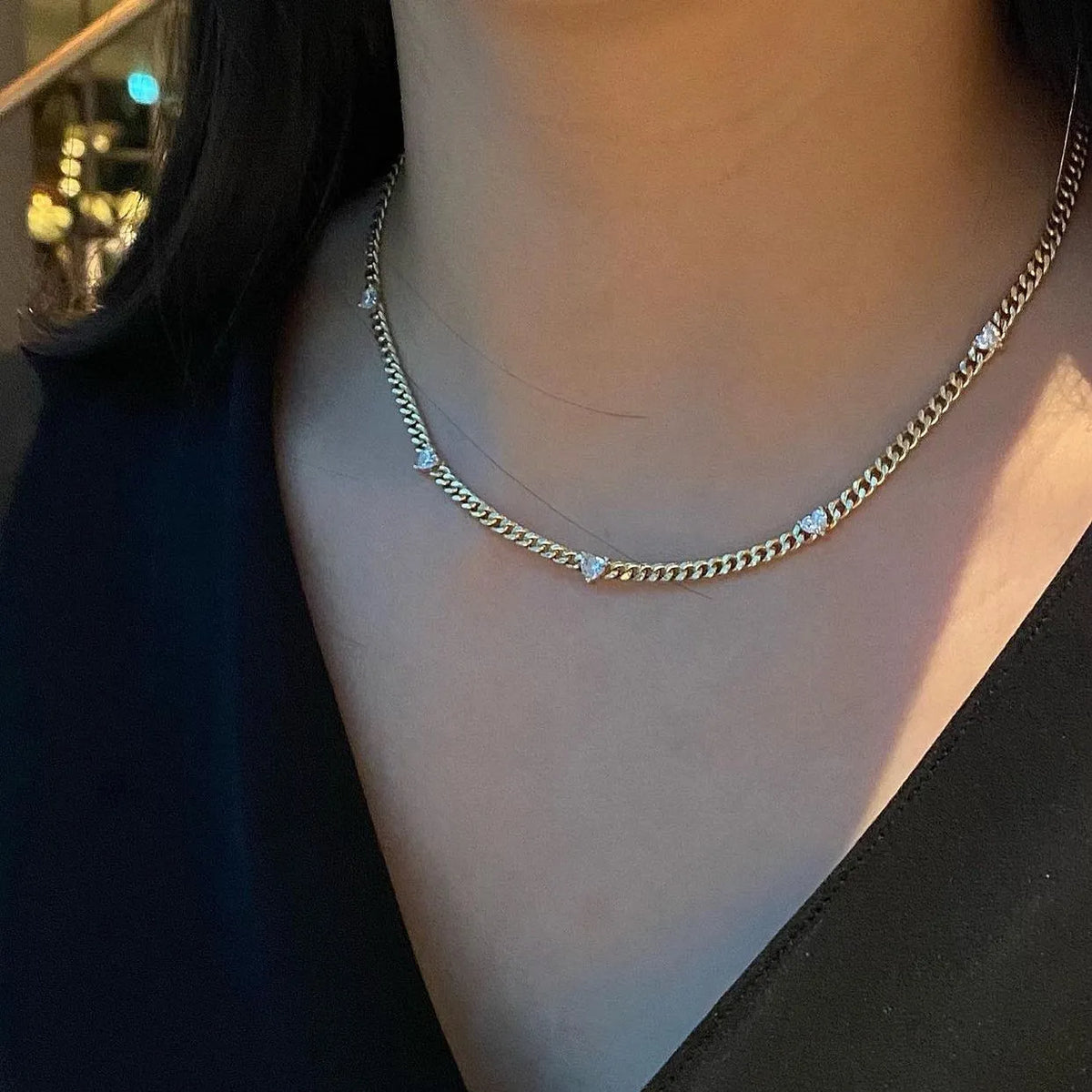 Gold chain necklace with small heart pendants on a person wearing a black top.