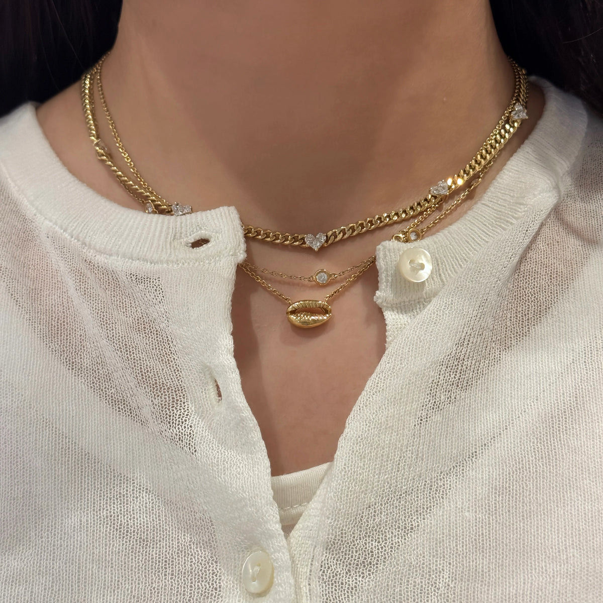 Close-up of a person wearing gold necklace styled with other necklaces with a white blouse.