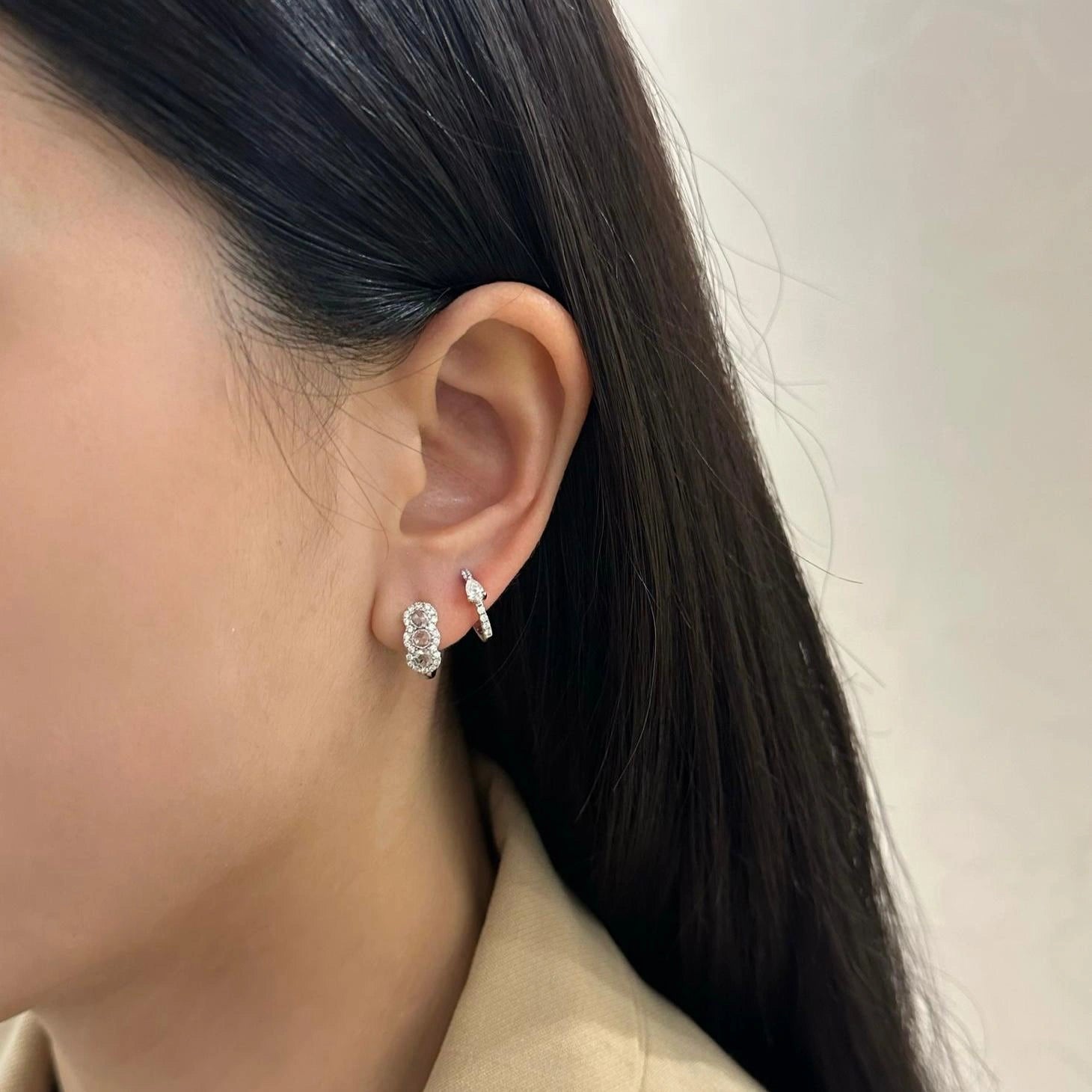 Close-up of a person wearing white gold diamond hoop earrings with neutral background