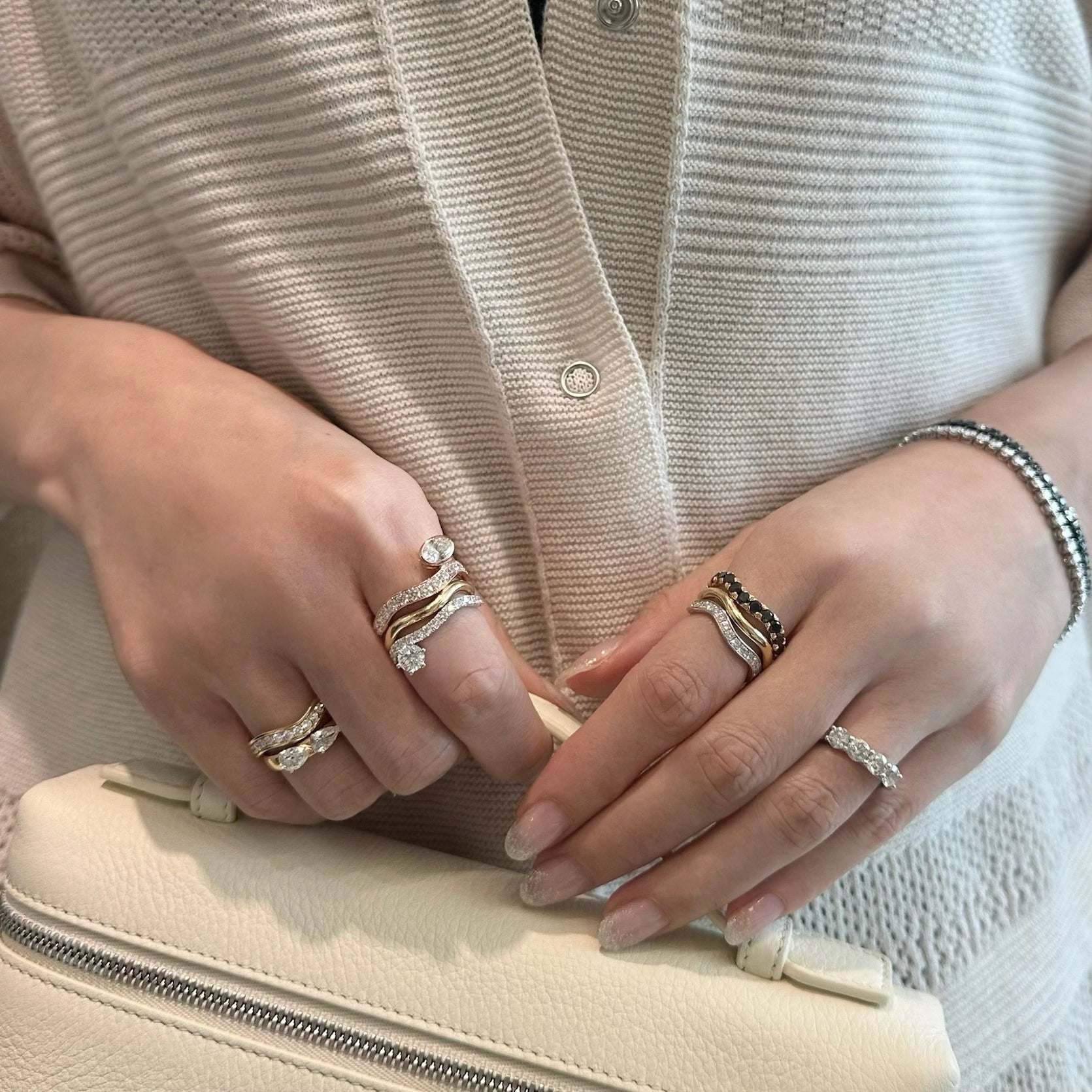 Close-up of hands with multiple rings on a beige clutch
