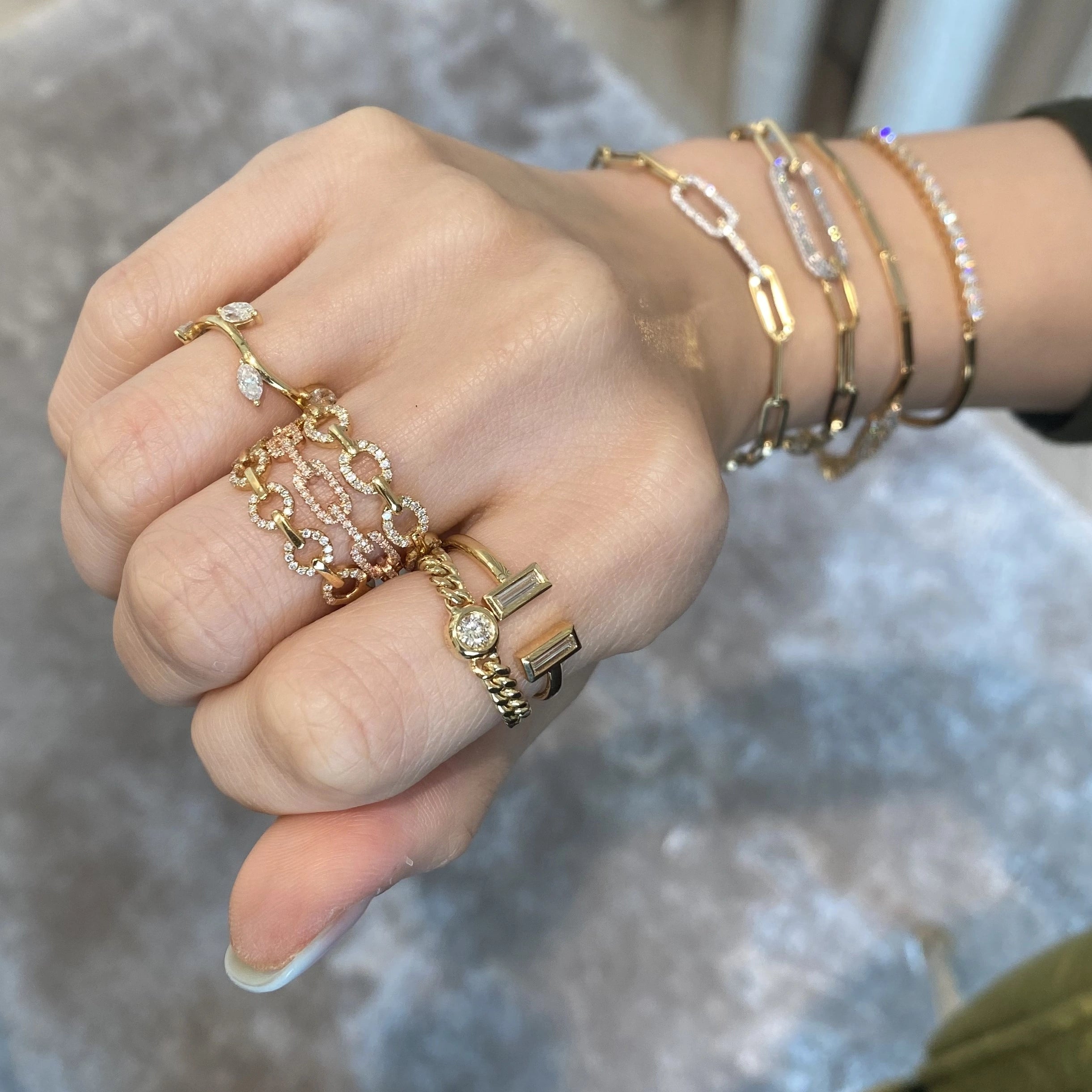 Hand wearing multiple gold rings and bracelets on a blurred background