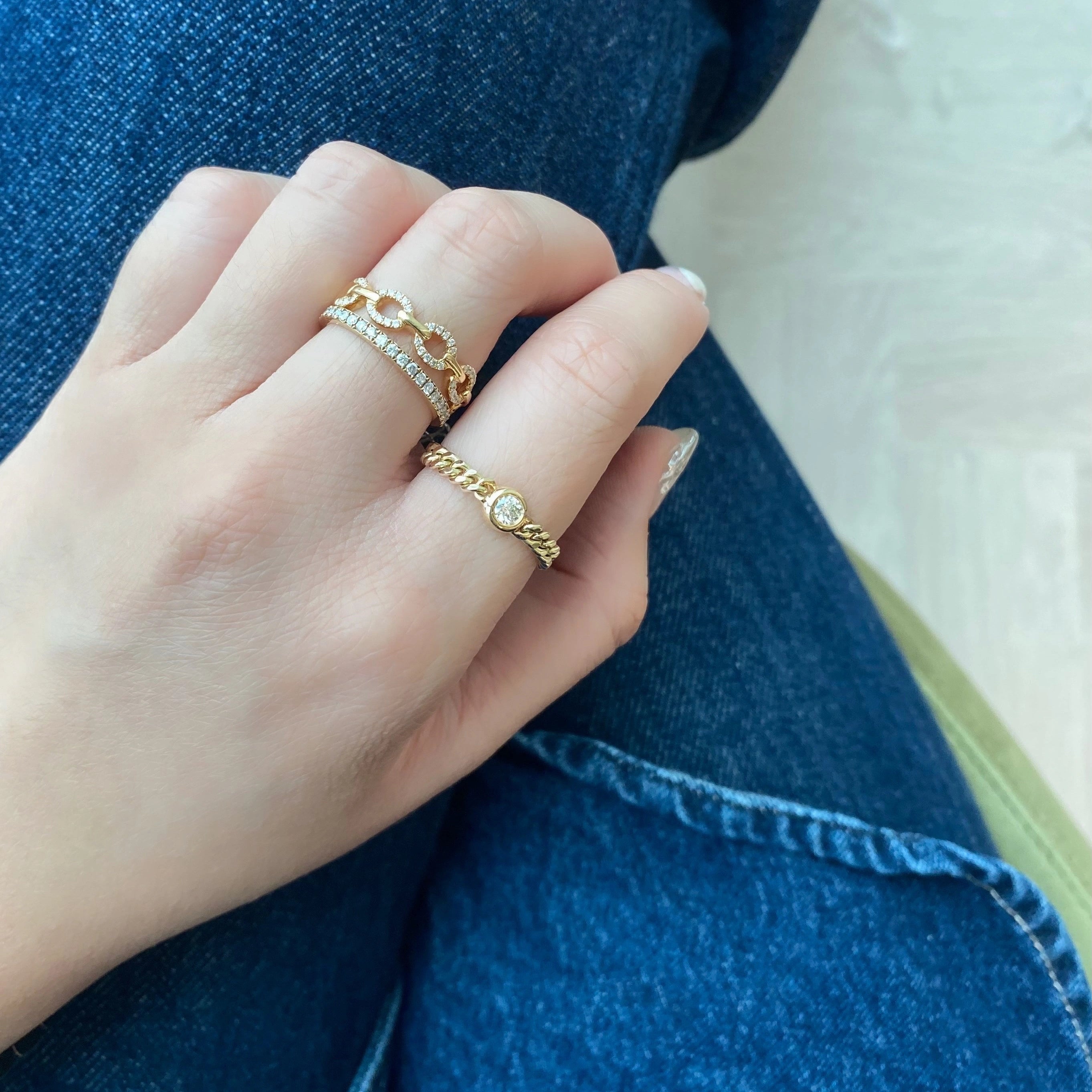 Hand wearing gold diamond rings with a blue denim background