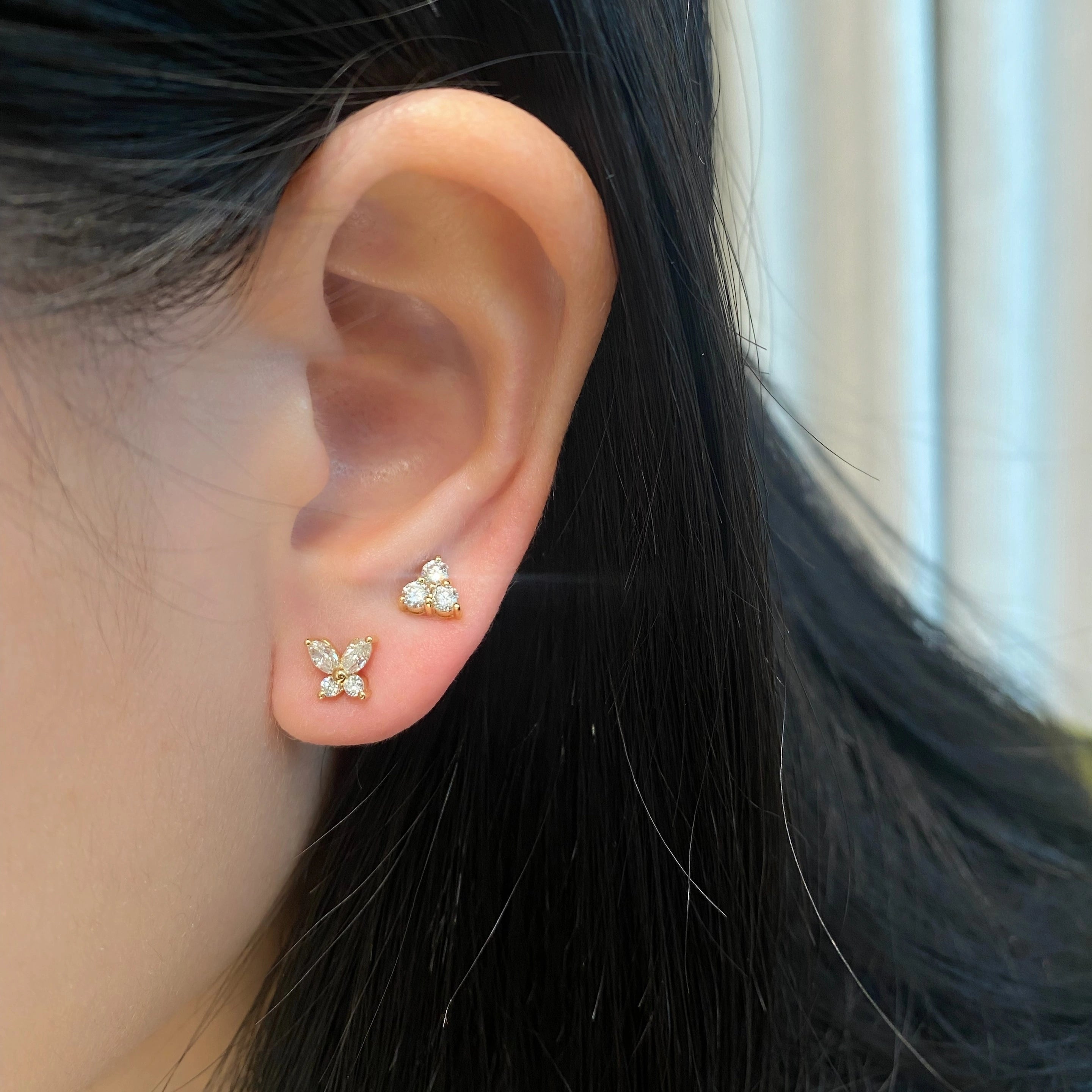 An ear wearing butterfly-shaped earrings & trio Studs